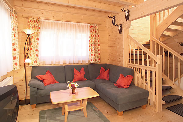 Wohnzimmer im Chalet Jagdhaus Wagrain mit grauem Ecksofa, roten Kissen, Holzwänden, Treppe und drei Hirschgeweihen an der Wand.