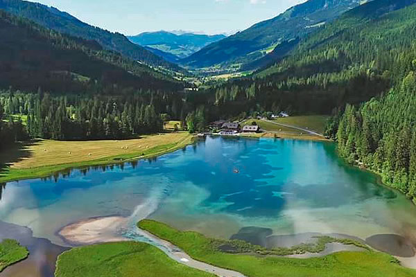 Bergsee mit türkisblauem Wasser, umgeben von Wiesen und Nadelwald, im Hintergrund bewaldete Berge und ein Tal bei Kleinarl.