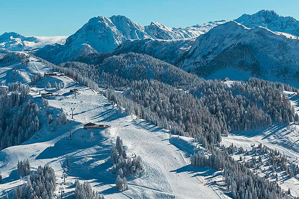 Verschneite Skipiste mit Skilift und Nadelbäumen vor Bergkulisse in Snow Space Salzburg.