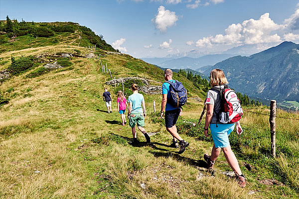 Gruppe von Wanderern mit Rucksäcken auf schmalem Pfad entlang eines grasbewachsenen Hangs in den Bergen bei Wagrain.